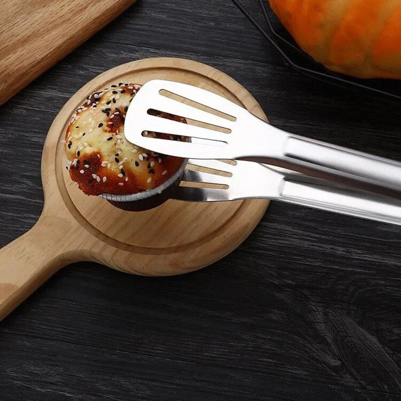 Stainless steel kitchen tongs holding a seeded muffin on a wooden board, Stel cookware