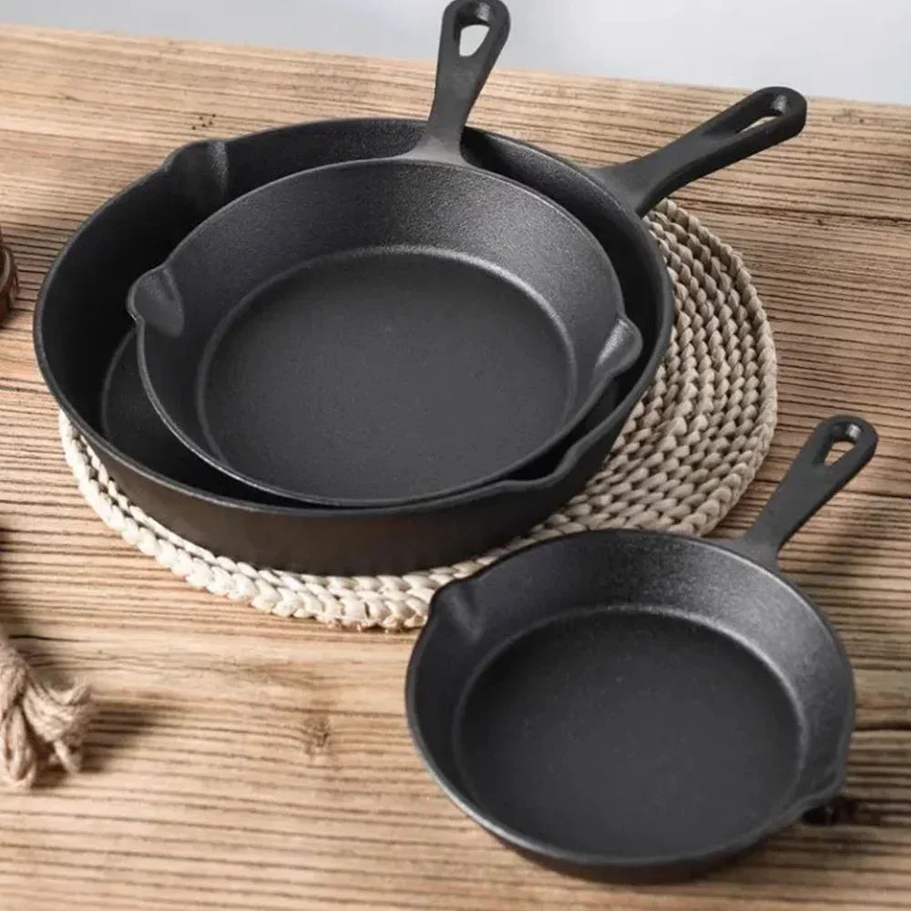 Three black cast iron skillets on a wooden table, plastic-free non-toxic cookware by STEL